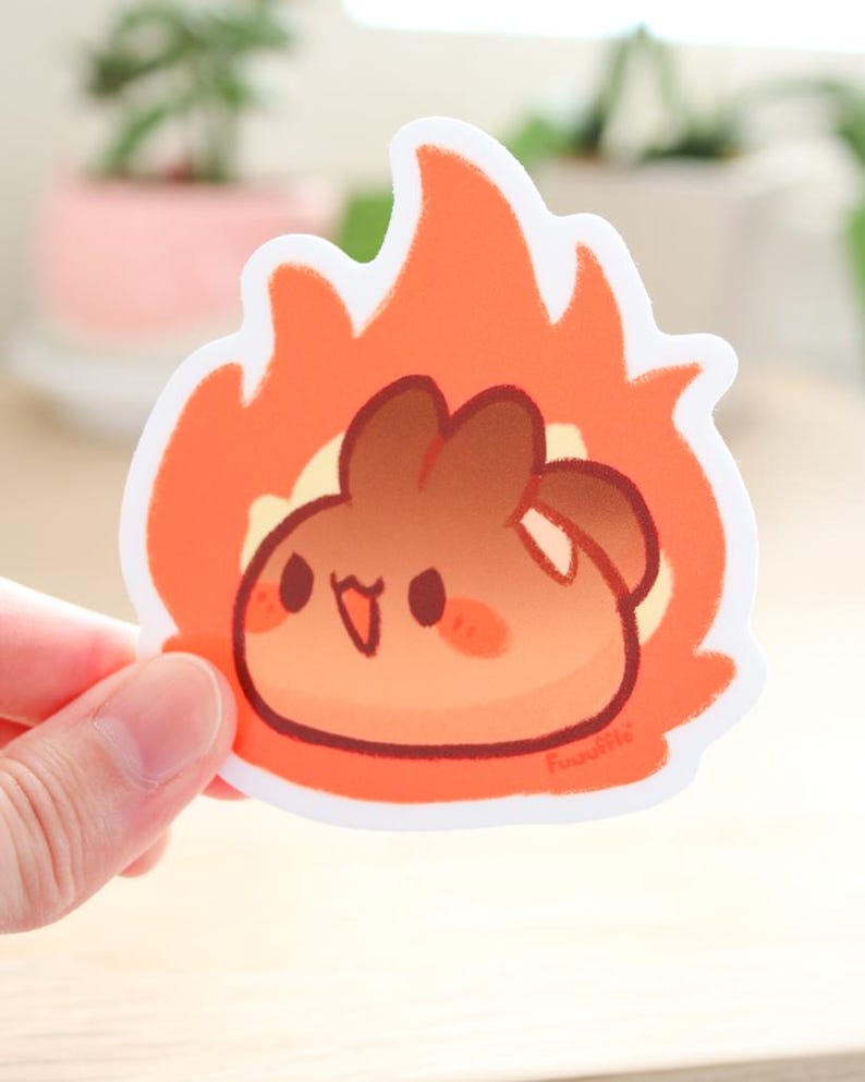 May include: A sticker of a brown cartoon character with a happy expression, set against a background of orange flames. The character has a round body and small arms and legs. The sticker is white with a white border.