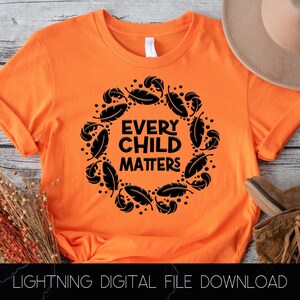 May include: Orange t-shirt with a black graphic design of a wreath of feathers with the text "Every Child Matters" in the center.