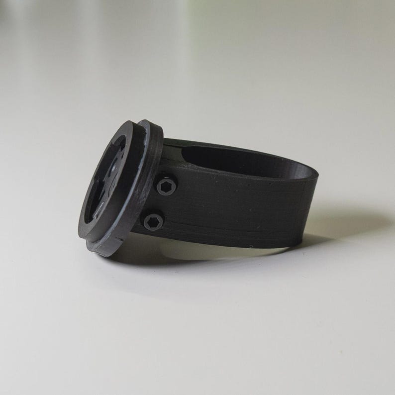Puede incluir: Soporte negro para ordenador de bicicleta, impreso en 3D. El soporte tiene una base circular con un &aacute;rea empotrada y dos tornillos peque&ntilde;os. La banda est&aacute; dise&ntilde;ada para envolver un manillar. El soporte es de material negro mate.