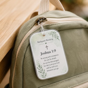 May include: A rectangular, semi-transparent acrylic tag attached to an olive green canvas backpack. The tag features a watercolor leaf design, a cross icon, and the text: Backpack Blessing, Joshua 1:9, Be strong and courageous.