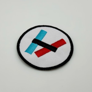 Può includere: Un cerotto circolare bianco con un bordo nero. Il cerotto presenta un design blu e rosso con una linea nera che interseca i due colori.