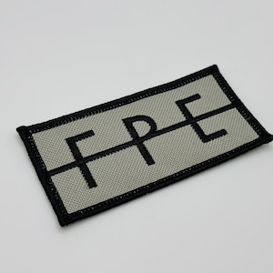 Può includere: Un cerotto in tessuto grigio con cuciture nere e la parola "FPE" ricamata in nero.