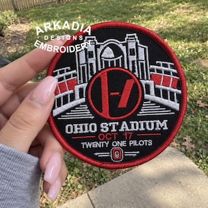 May include: A circular embroidered patch featuring a black background with a red border. The design depicts the Ohio Stadium in white and red thread, a central red circle with a black Twenty One Pilots logo, and text reading OHIO STADIUM, OCT 17, TWENTY ONE PILOTS.