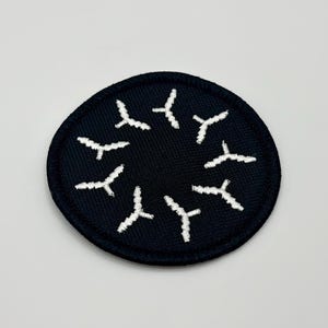 May include: A black circular patch with a white embroidered design of multiple stylised airplane shapes arranged in a circle.