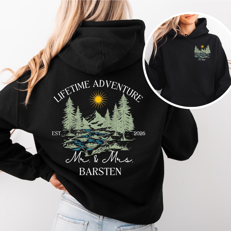 May include: Black hoodie with a landscape design on the back, including trees, a river, mountains, and a sun. The text reads "LIFETIME ADVENTURE" above the design, with "Mr. & Mrs. BARSTEN" below. A smaller version of the design is on the front.