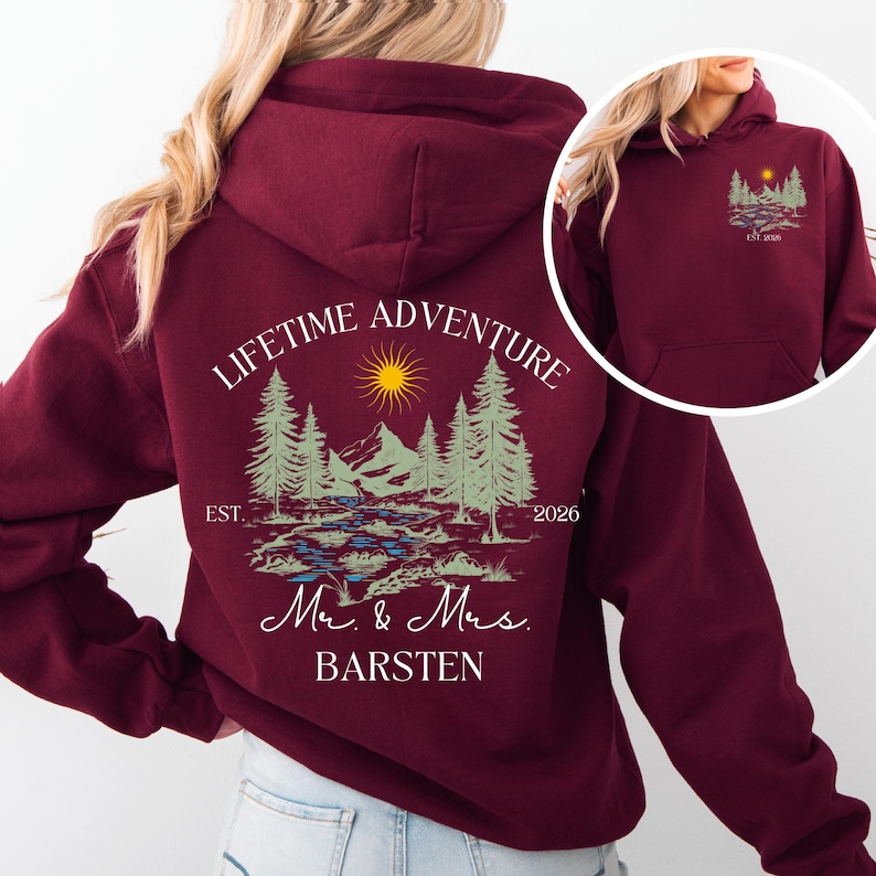 May include: Burgundy hoodie with a landscape design featuring trees, mountains, a river, and a sun. The back of the hoodie reads "LIFETIME ADVENTURE" above the landscape, with "Mr. & Mrs. BARSTEN" below. The front has a smaller version of the design.