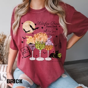 May include: A red t-shirt with a graphic of a witch's brew, a black cat, and a guest check that says "Witches Brew Guest Check" and "Pick Your Poison".
