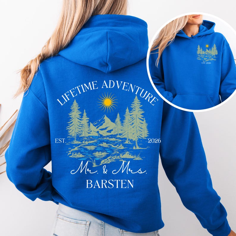 May include: A royal blue hoodie featuring a nature-themed design. The graphic includes a sun, mountains, trees, and the text "LIFETIME ADVENTURE" and "Mr. & Mrs. BARSTEN". The year "2026" is also displayed.