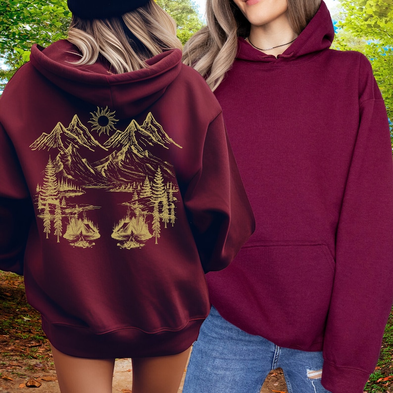 May include: Two maroon hoodies, one with a gold mountain scene graphic on the back. The graphic features mountains, trees, a lake, and a sun.