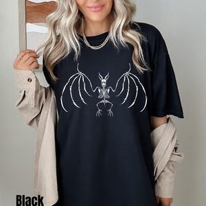 Puede incluir: Camiseta negra con un gráfico blanco de un esqueleto de murciélago con las alas extendidas.