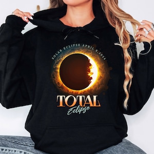 May include: Black hoodie with a graphic of a solar eclipse with the text "SOLAR ECLIPSE APRIL 8, 2024 TOTAL Eclipse".