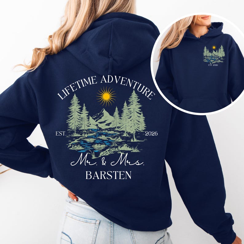 May include: A navy blue hoodie with a landscape design featuring trees, mountains, and a sun. The text "LIFETIME ADVENTURE" arches above the design, with "Mr. & Mrs. BARSTEN" below. A smaller version of the design is on the front.