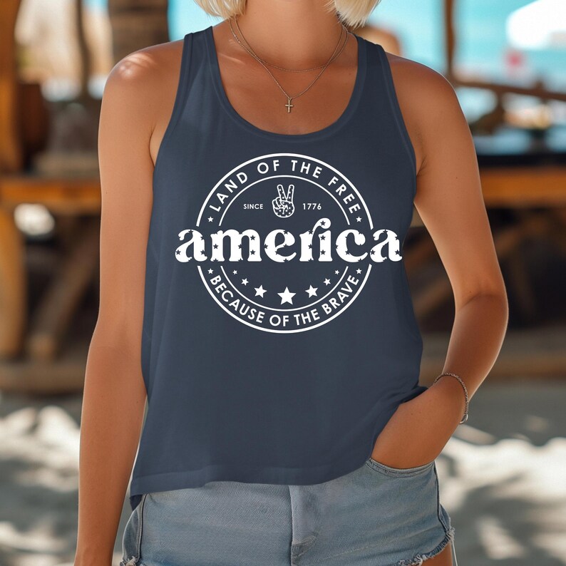 Pode incluir: Top sem mangas azul marinho com um design circular branco que diz "Land of the Free" e "America", com um sinal de paz e estrelas. Inclui tamb&eacute;m a frase "Because of the Brave". O top &eacute; sem mangas.