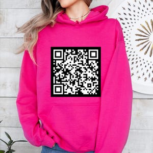 Peut inclure: Un sweat à capuche rose vif avec un code QR noir et blanc imprimé sur le devant.
