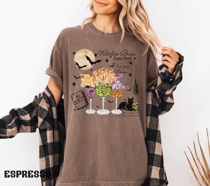 May include: A brown t-shirt with a graphic of three witches' brew cocktails, a black cat, and the text "Witches Brew Guest Check Pick Your Poison".
