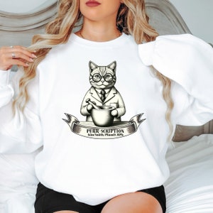 Puede incluir: Sudadera blanca con una ilustración en blanco y negro de un gato con gafas y bata de laboratorio sosteniendo un mortero y un pilón. El texto "PURR-SCRIPTION Kim Smith, Pharm.D., RPh." está debajo de la ilustración.