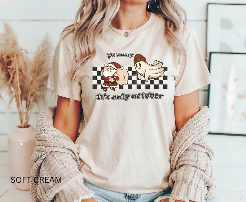May include: A cream-colored t-shirt with a graphic of a ghost chasing Santa Claus away with the text "Go away it's only October".