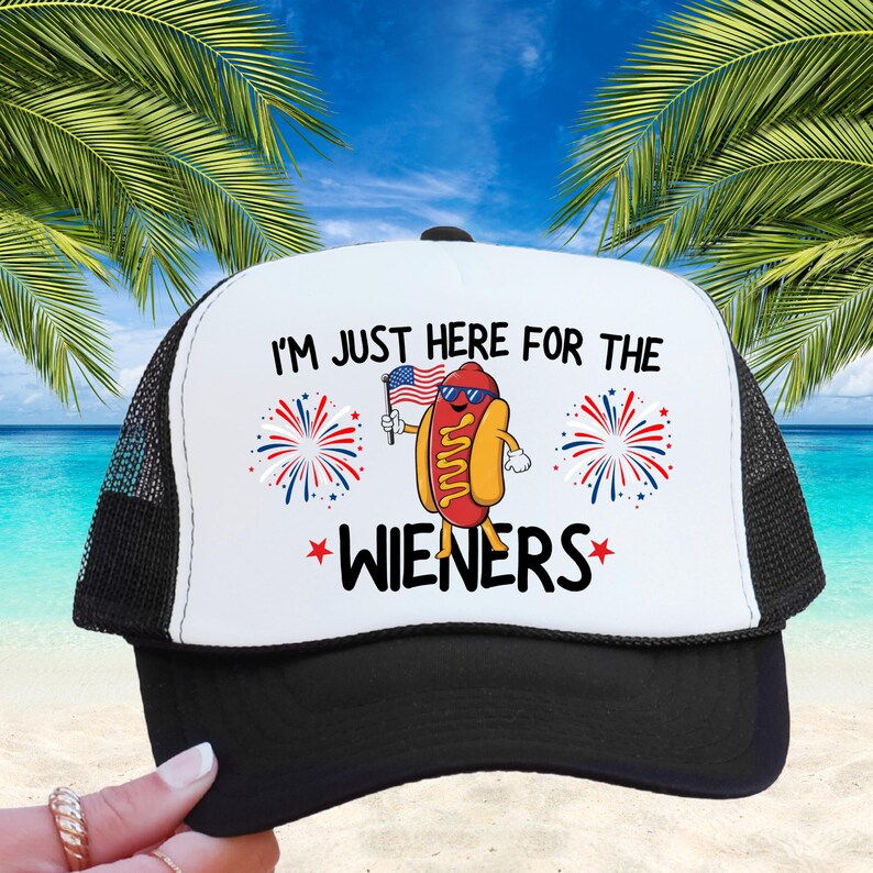 Puede incluir: Una gorra de camionero blanca y negra con una bandera estadounidense roja, blanca y azul y un perro caliente de dibujos animados sosteniendo la bandera. El texto en la gorra dice "I'm just here for the wieners".