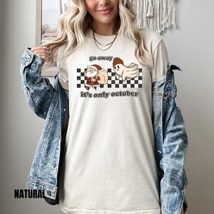 May include: A white t-shirt with a black and white checkered pattern, a cartoon ghost, and a cartoon Santa Claus. The text on the shirt reads "go away it's only october".