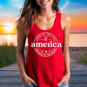 Pode incluir: Uma regata vermelha com um gr&aacute;fico circular branco que diz "LAND OF THE FREE" e "america" com estrelas e o texto "BECAUSE OF THE BRAVE."
