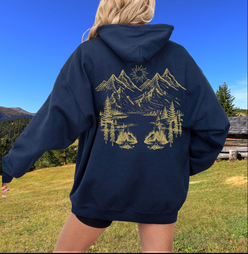 May include: A navy blue hooded sweatshirt with a gold mountain scene on the back. The scene includes mountains, a lake, trees, and a campfire.