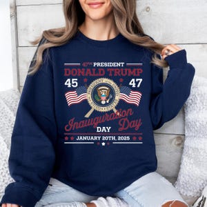 以下が含まれることがあります： 紺色の長袖スウェットシャツ。グラフィックデザインには、「47th President Donald Trump 45 47 Inauguration Day January 20th, 2025」の文字と、大統領の紋章、アメリカの国旗2つが描かれている。