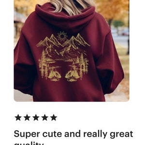 May include: A maroon hoodie with a gold mountain scene graphic on the back. The graphic features mountains, a lake, trees, and a sun.
