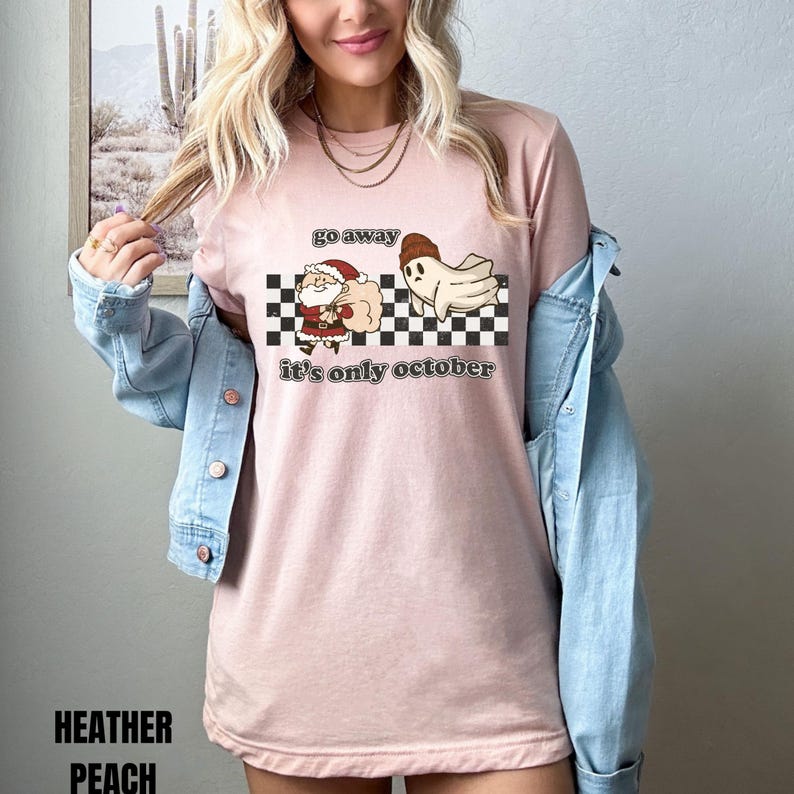 May include: A pink t-shirt with a black and white checkered background. The shirt has a graphic of a ghost chasing Santa Claus away with the text "go away it's only october".