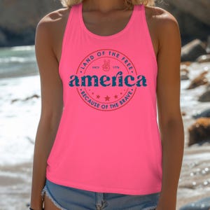 Pode incluir: Regata rosa brilhante com um gr&aacute;fico redondo que diz "Land of the Free" e "America" em azul, com um sinal de paz e estrelas. O texto "Because of the Brave" tamb&eacute;m est&aacute; inclu&iacute;do. A regata &eacute; sem mangas.