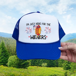 Puede incluir: Una gorra de camionero azul y blanca con el texto "Solo estoy aqu&iacute; por las salchichas" y un dibujo animado de un perrito caliente sosteniendo una bandera estadounidense.