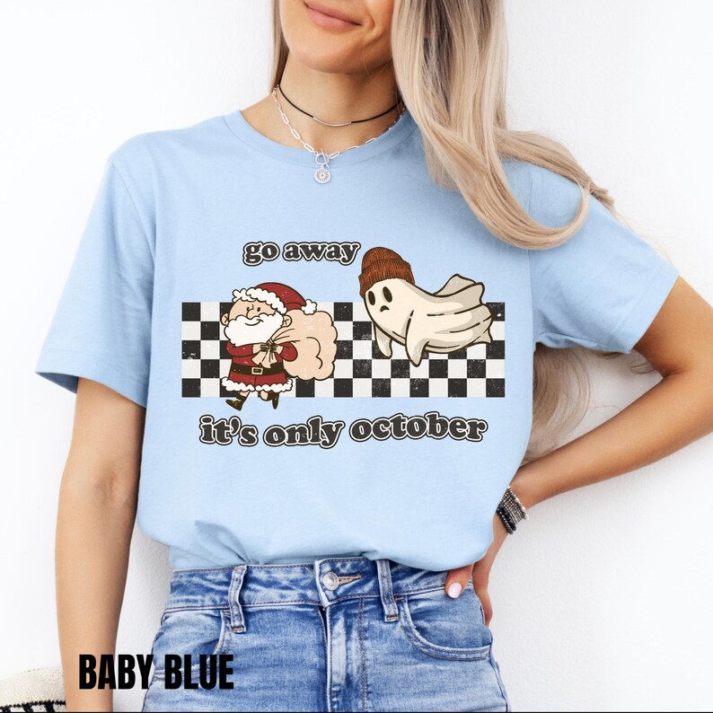 May include: A light blue t-shirt with a checkered background and a ghost chasing Santa Claus. The text on the shirt reads "go away it's only october".