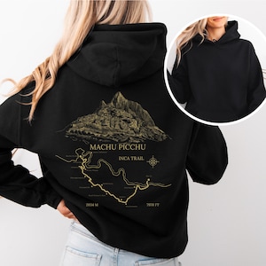 Puede incluir: Sudadera con capucha negra con una ilustración dorada de Machu Picchu y el Camino Inca. El diseño incluye el texto "Machu Picchu" e "Inca Trail", con medidas de 2034 m y 7970 ft. La sudadera tiene capucha y bolsillo delantero.