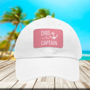 May include: White baseball cap with a pink patch that says "DIBS on the CAPTAIN" with an anchor graphic.