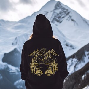 May include: Black hooded sweatshirt with a gold mountain scene graphic on the back. The graphic features mountains, a sun, trees, and a lake.