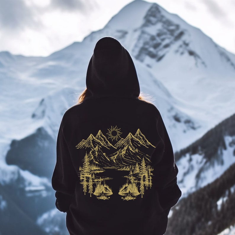 May include: Black hooded sweatshirt with a gold mountain scene graphic on the back. The graphic features mountains, a sun, trees, and a lake.