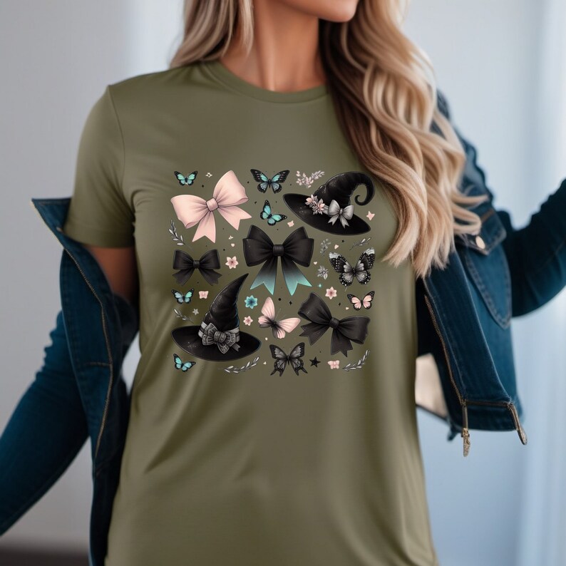 Pode incluir: Uma camiseta verde com uma estampa de chap&eacute;us de bruxa pretos, la&ccedil;os rosa e azuis e borboletas. O design est&aacute; centralizado na camiseta.