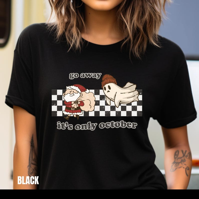 May include: Black t-shirt with a white and black checkered background. The text "go away it's only october" is printed on the shirt. A cartoon ghost wearing a hat is running away from a cartoon Santa Claus.
