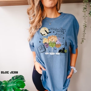 May include: A blue t-shirt with a graphic of three witches' brew cocktails, a black cat, and the text "Witches Brew Guest Check Pick Your Potion Salem Massachusetts".