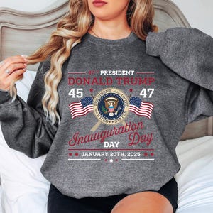 以下が含まれることがあります： 大統領の紋章と「第47代大統領ドナルド・トランプ 45 47 就任式の日 2025年1月20日」というテキストがプリントされたグレーのスウェットシャツ。
