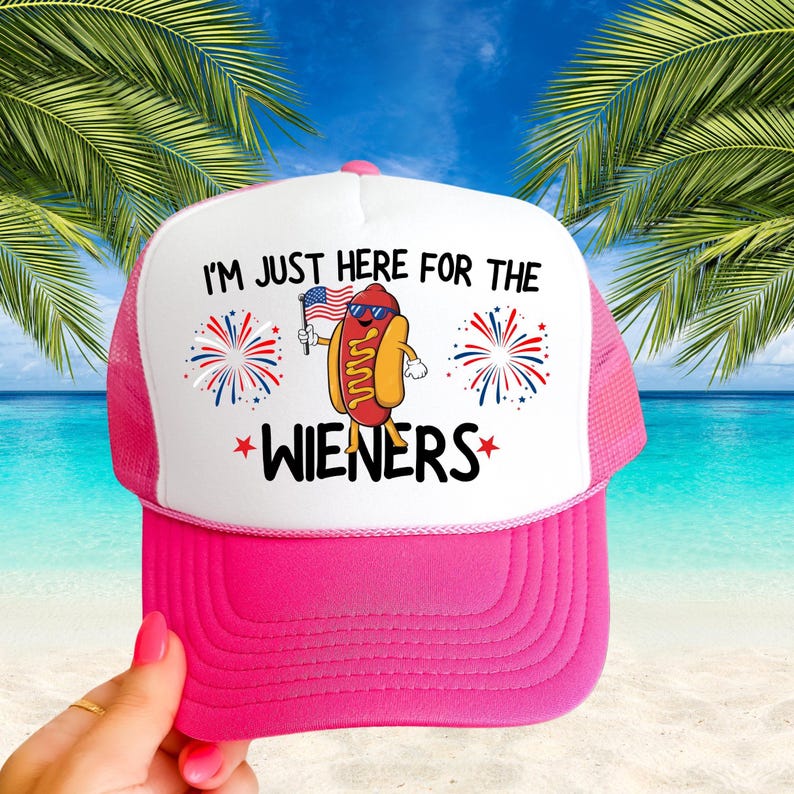 Puede incluir: Gorra de camionero rosa y blanca con un dibujo animado de un perrito caliente con gafas de sol y sosteniendo una bandera estadounidense. El texto en la gorra dice "I'm just here for the wieners".