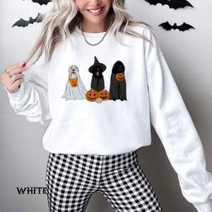 May include: White sweatshirt featuring a Halloween-themed graphic. The design includes three dogs dressed as a ghost, a witch, and a vampire, each holding a jack-o'-lantern. The word "WHITE" is printed at the bottom of the sweatshirt.