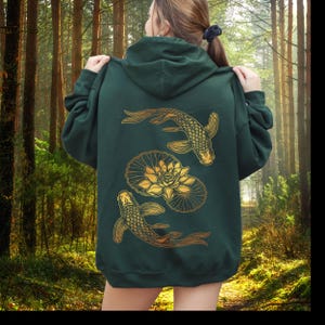 May include: A dark green hoodie with a gold design of two koi fish swimming around a lotus flower. The hoodie has a drawstring hood and a front pouch pocket.