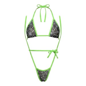 Puede incluir: Un conjunto de bikini negro y verde neón. La parte superior e inferior del bikini son negras con un diseño de telaraña blanca. Los bordes y las correas son de color verde neón, con cierres de lazo en el cuello, la espalda y las caderas.