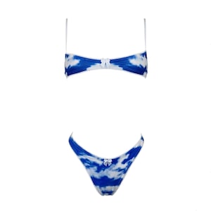 Puede incluir: Conjunto de lencería de dos piezas con un diseño de nubes azules y blancas. La parte superior es un bralette con tirantes finos y un pequeño lazo en el centro. La parte inferior a juego es un tanga, también con un lazo. El conjunto tiene ribetes de encaje blanco.
