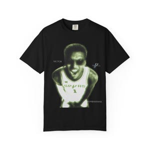 以下が含まれることがあります： 黒いTシャツ。ネオングリーンのスパーズのジャージを着たバスケットボール選手の画像がプリントされています。選手の名前「Victor」が画像の上に、そして「Wembanyama」が下に印刷されています。背番号「1」が見えます。
