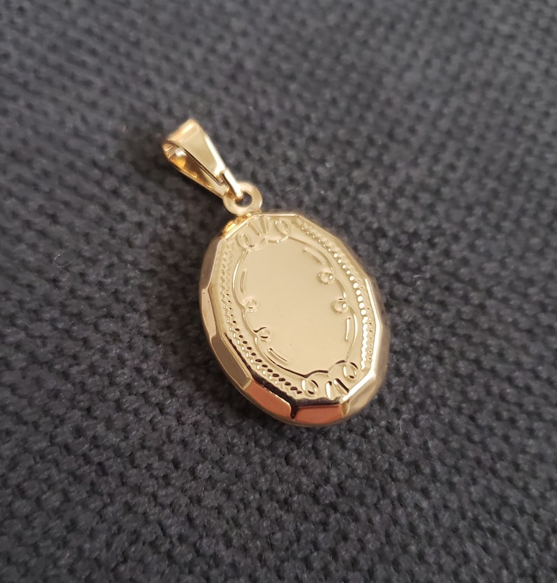 May include: A gold oval locket with a detailed engraved design around the edge.