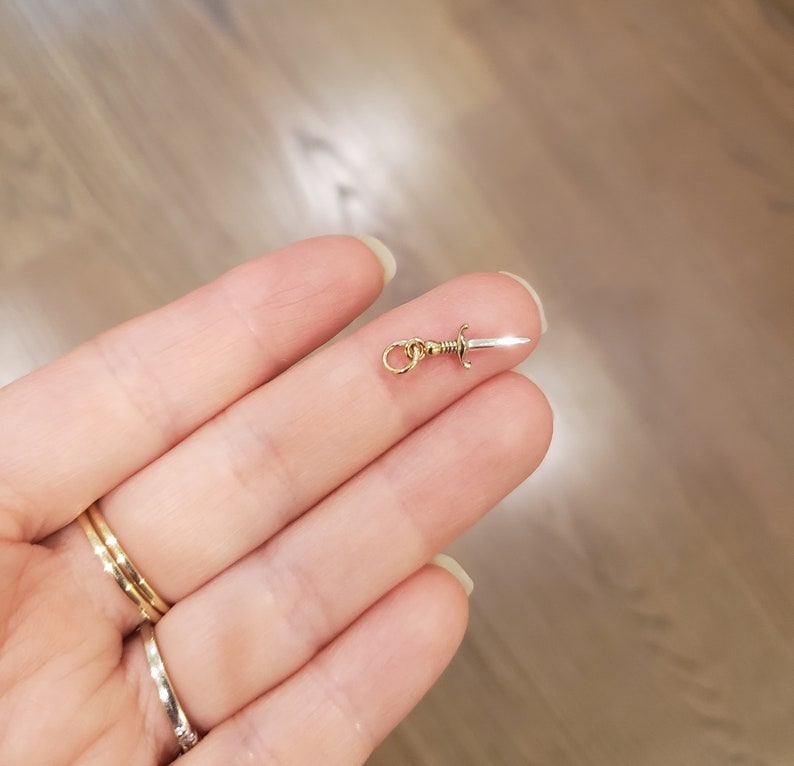 Peut inclure: Un charme en or en forme de dague argent&eacute;e avec une boucle dor&eacute;e pour l'attacher &agrave; un collier ou un bracelet.