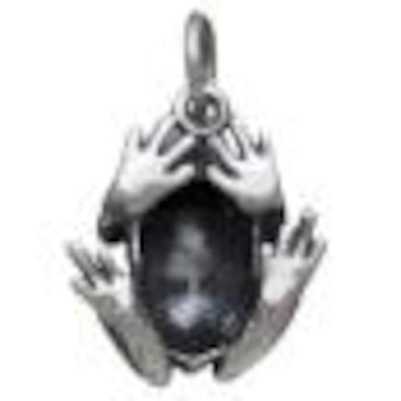 May include: A silver-toned pendant in the shape of a frog, with hands raised to its face. The frog's body is a dark, oval-shaped stone. The pendant has a loop at the top for a chain.