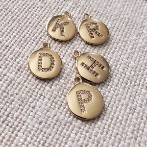 Puede incluir: Cinco dijes de metal dorado con un diseño de letra de cristal transparente. Las letras son K, R, D, H y P.