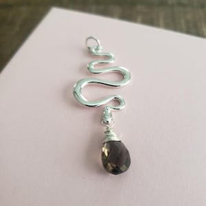 May include: A silver snake pendant with a dark brown gemstone hanging from it. The snake is curled in a spiral shape.